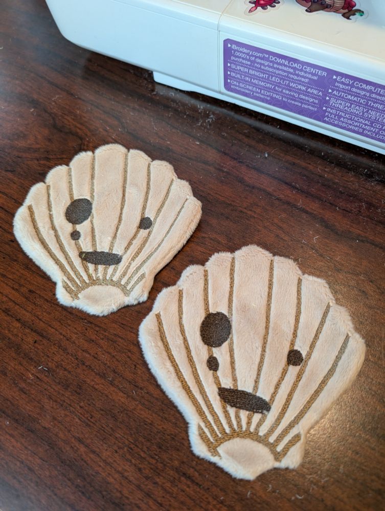 WIP of two handmade Ocean Korok plushies from the Legend of Zelda.  Shows the embroidered masks on a table.
