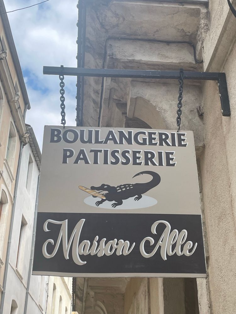 Sign: as well as a crocodile with a baguette, it says ‘Boulangerie Patisserie Maison Alle’. 