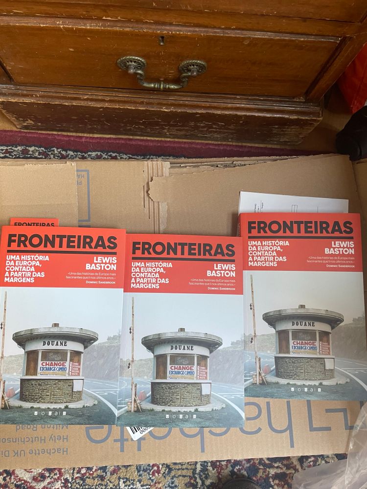 Three copies of the book, titled ‘Fronteiras’. The cover illustration is of a border post in the mist. 