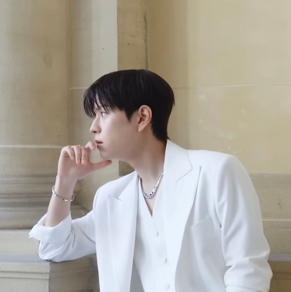 Picture of Seungmin from his visit to Paris captured from his mini vlog about the trip. It shows the shooting of the picture previously
He is wearing a white three-piece suit (no shirt 😳) and leaning with one elbow on a pillar.
The entire scene his heavily filtered to make his complexion appear lighter.
