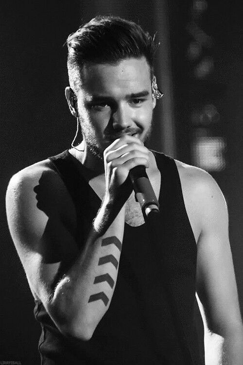 Black and white photo of Liam Payne wearing a black tank top and singing on stage