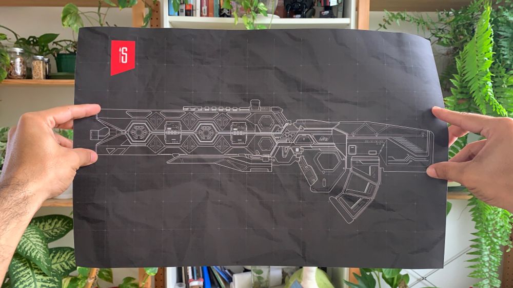 My two hands holding a poster of a schematic illustration of the Heat Sink legendary skin for the Flatline weapon from Apex Legends. There is a indoor garden in the background.