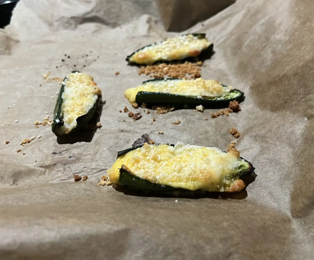 Four roasted jalapeno halves stuffed with glistening melted cheese and topped with golden-brown panko, on parchment paper