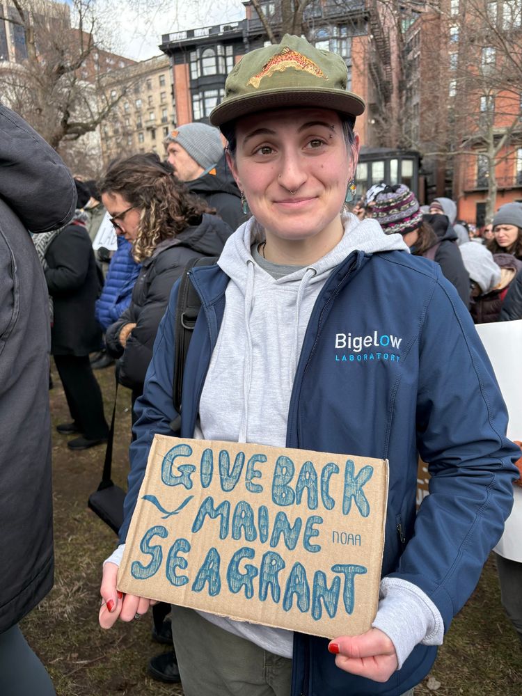 A person holds a sign saying “give back Maine Sea Grant”