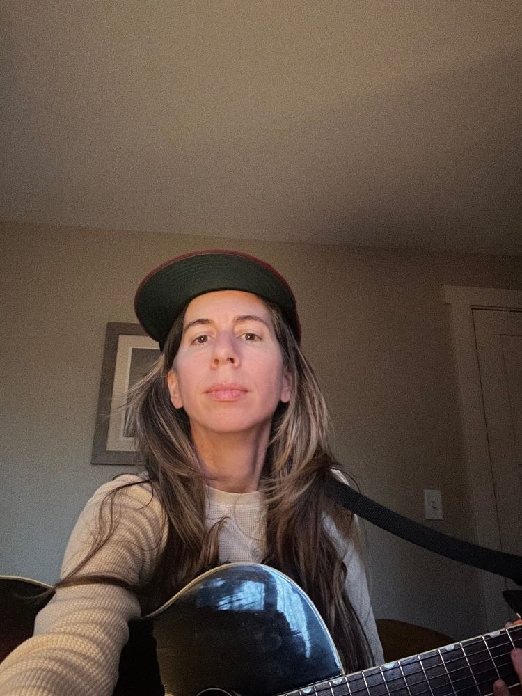 I'm staring into camera, soft look, guitar in hand, silk green lining on baseball cap rim.