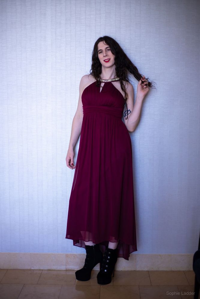 Sophie standing in a burgundy dress and black heels, playing with her hair with one hand