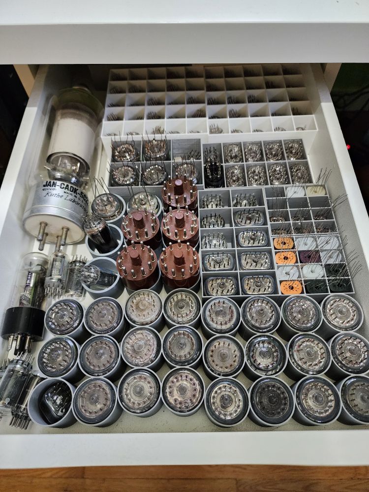 A white drawer filled with over a hundred small vacuum tubes sorted out into 3d printed holders.