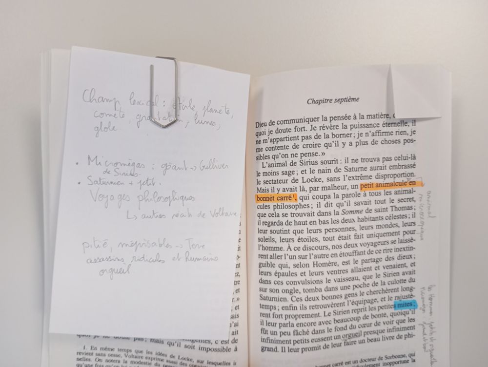 Livre de Voltaire avec notes de lecture inscrites sur une feuille accrochée avec un trombone.