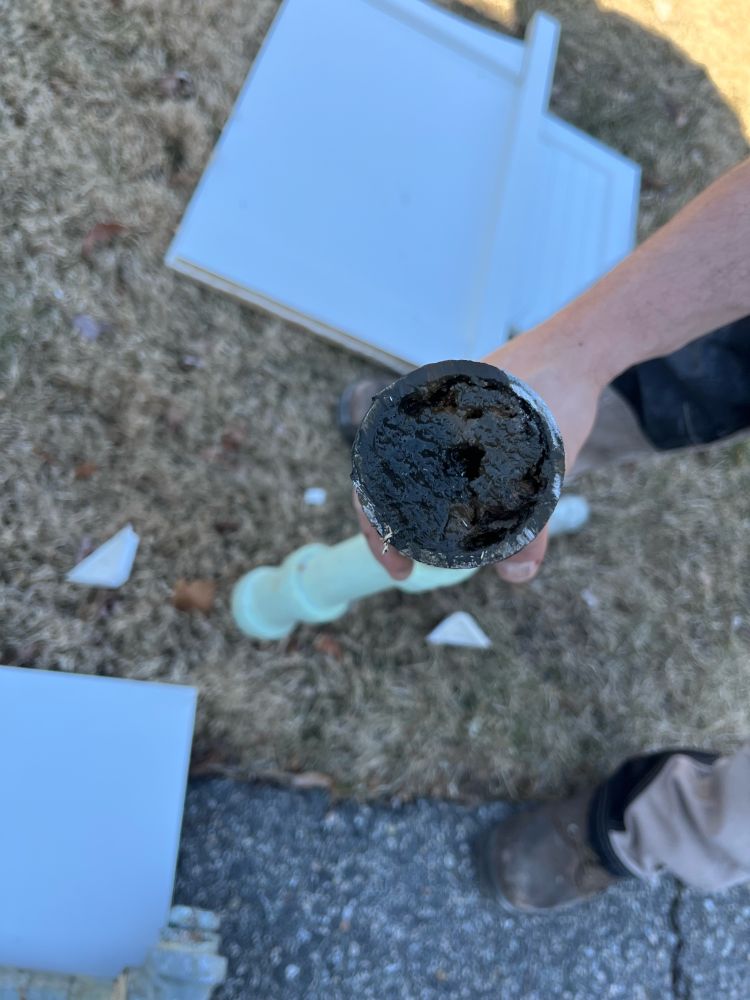 A hand holding an iron pipe that is entirely clogged with sediment and rust. 