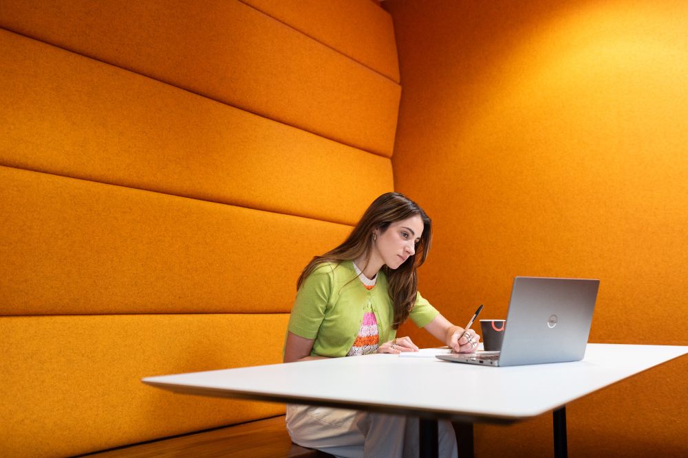 A student working on a laptop against a vibrant orange background. 