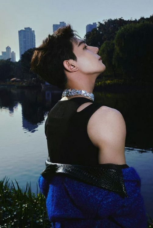 Pic of Xia Zhiguang taken from behind him, in a black tank top wearing a wide, sparkly collar/necklace/choker 