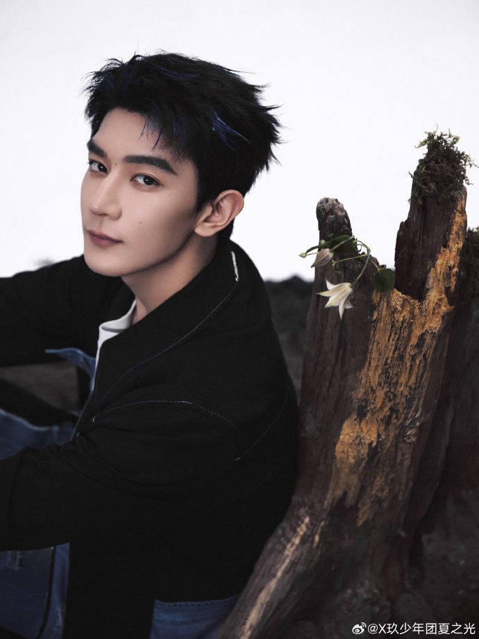 Xia Zhiguang leaning against a stump looking over his shoulder at the camera