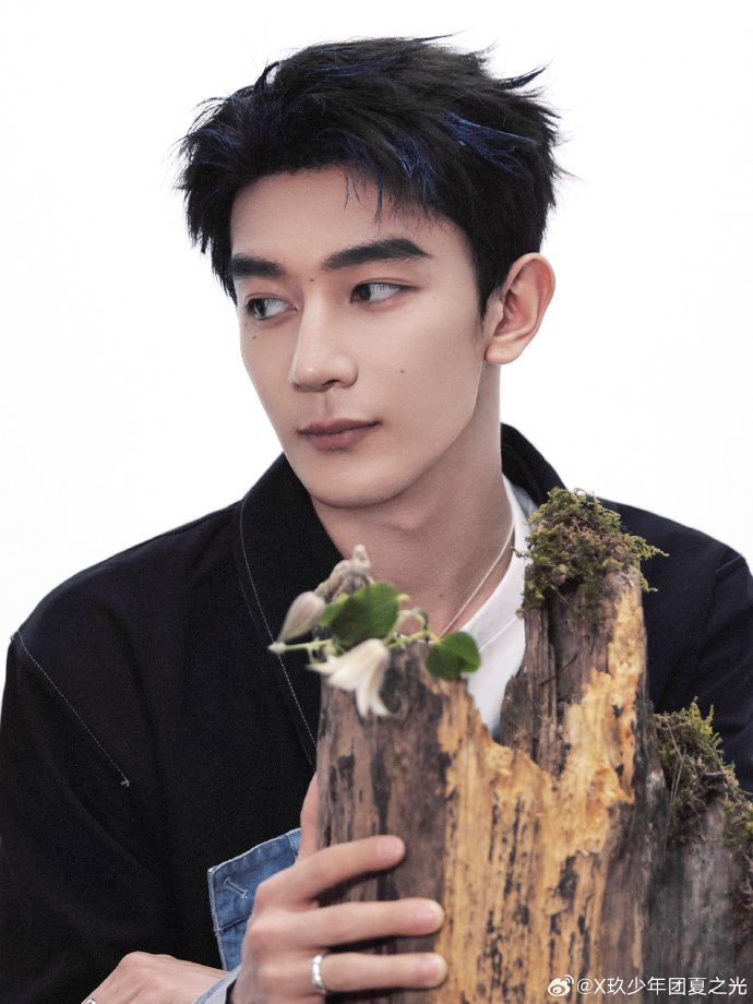 Xia Zhiguang sitting behind a stump, reaching forward to hold it with his hand 