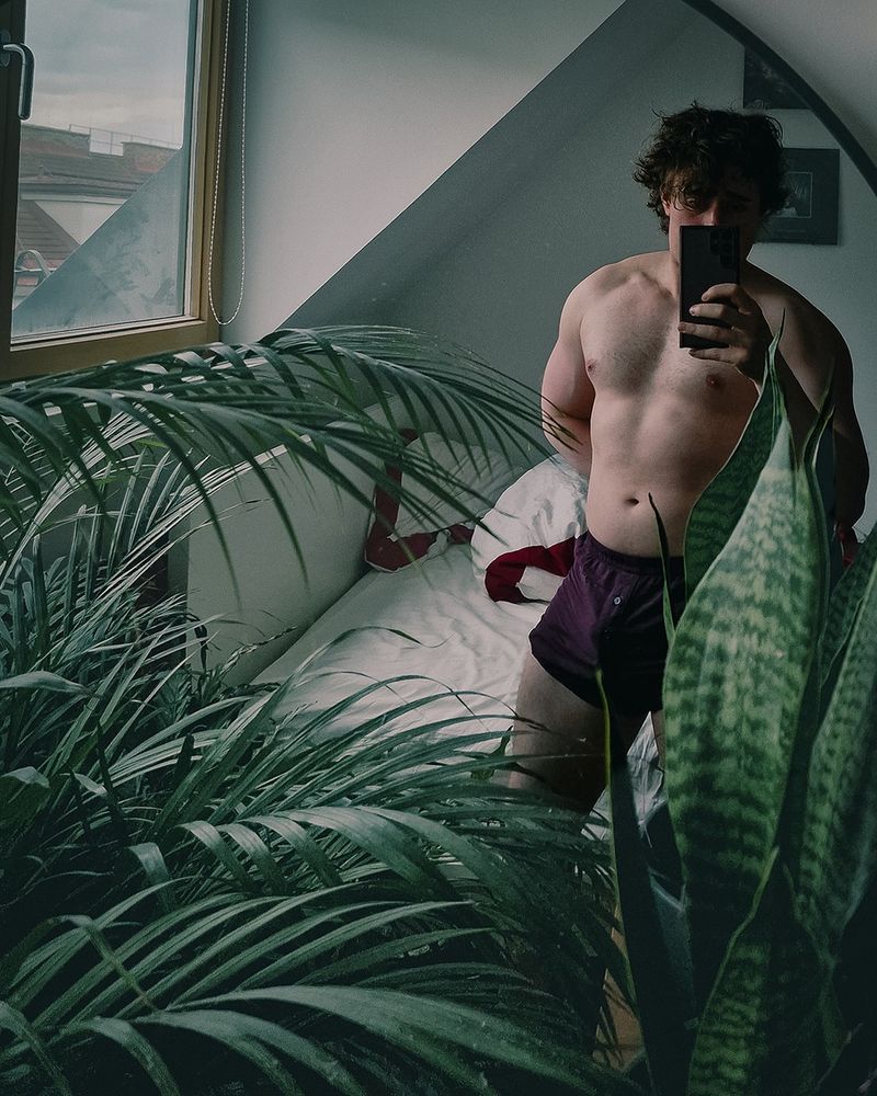 Mirror selfie in boxer shorts with a slight peak of the biceps vein behind the pecs