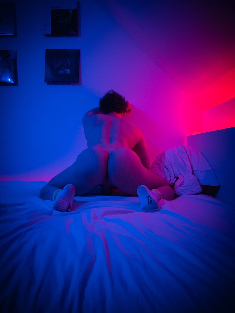 Muscular guy in doggy pose, leaned against the wall in red and blue moody light.