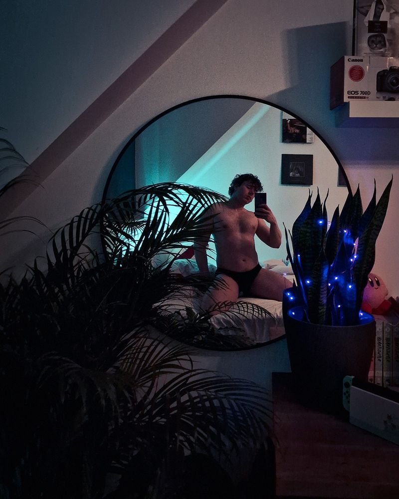 Mirror selfie showing off pecs in gloomy cyan to purple light