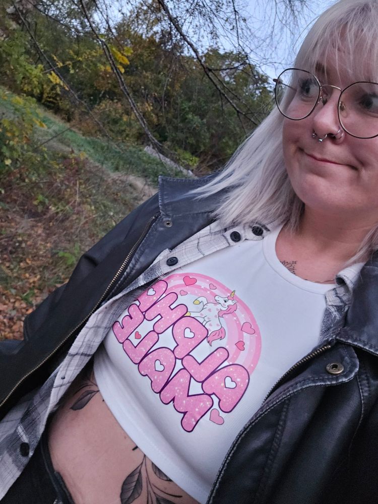 Bilde tatt av megselv ute på tur, jeg har på meg en croptop med Alpha Male i rosa med enhjørning og hjerter, flannelskjorte og oversized skinnjakke, med synlig midlinje hvor bladene på den nye tatoveringa er synlig  