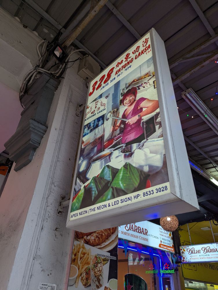 328 Katong Laksaの看板。女性が厨房で料理をしているイラストが描かれている。