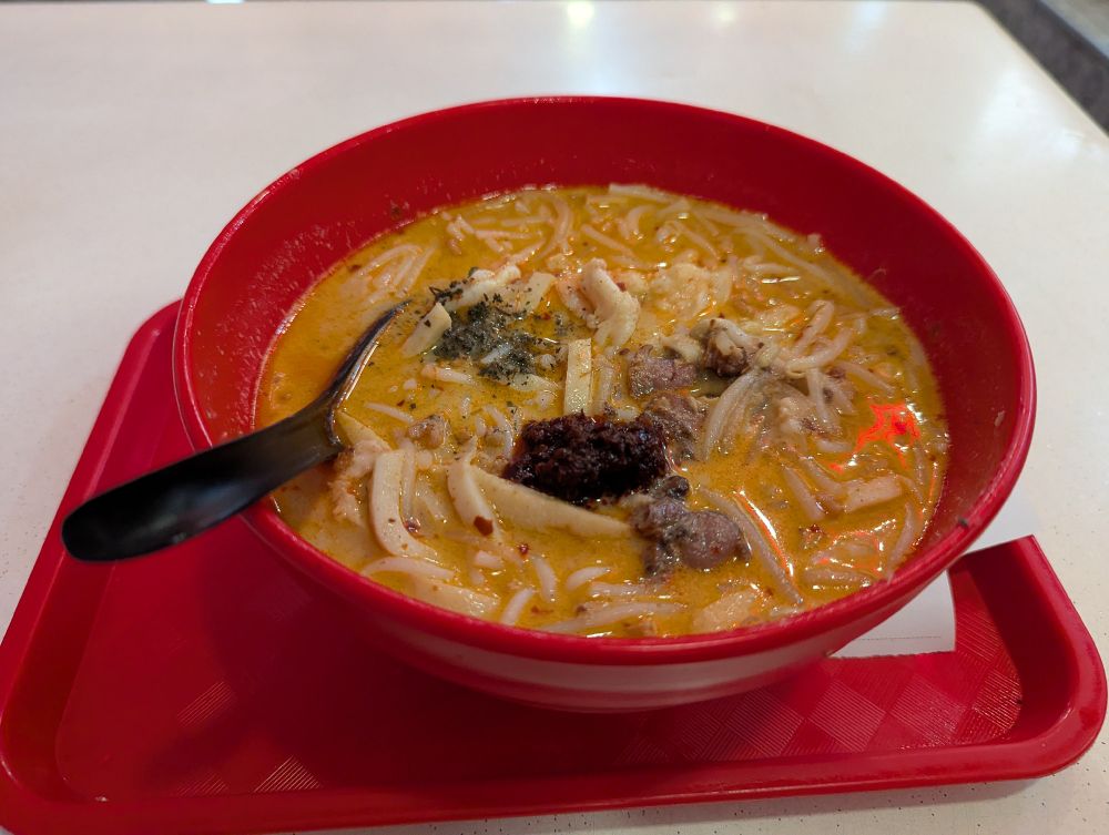 ラクサの写真。赤いどんぶりの中に麺やかまぼこが入っている。