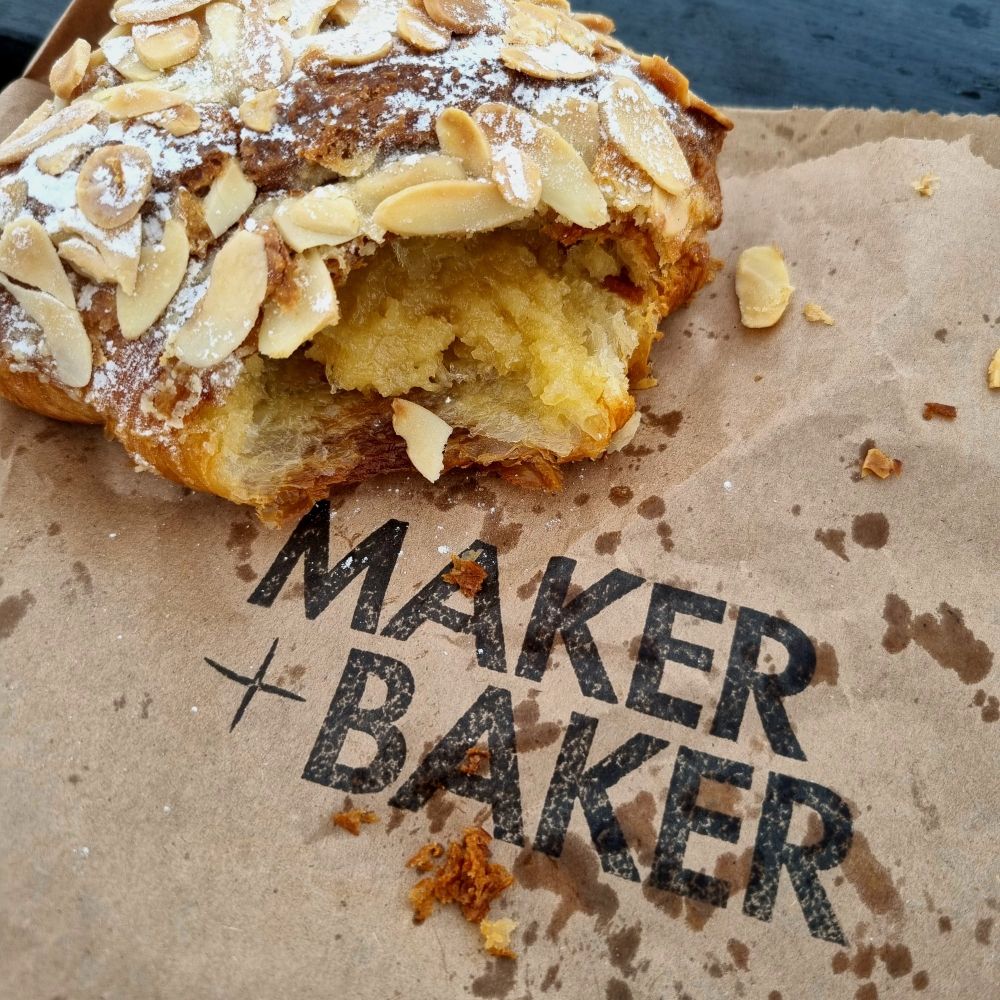 Picture of an tore up almond croissant on top of a paper bag with the logo Maker + Baker