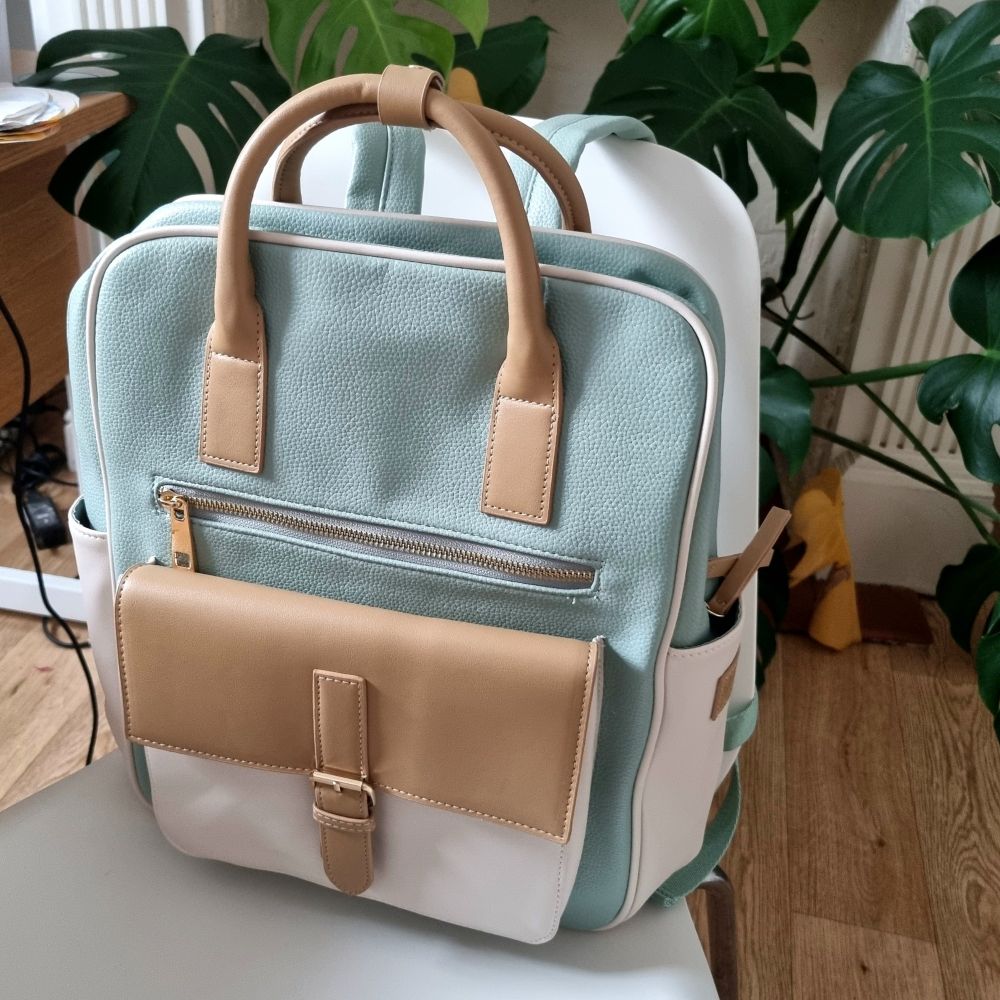 Picture of a gorgeous turquoise backpack with tan handles, white side pouches, and front pocket with tan flap cover ❤️