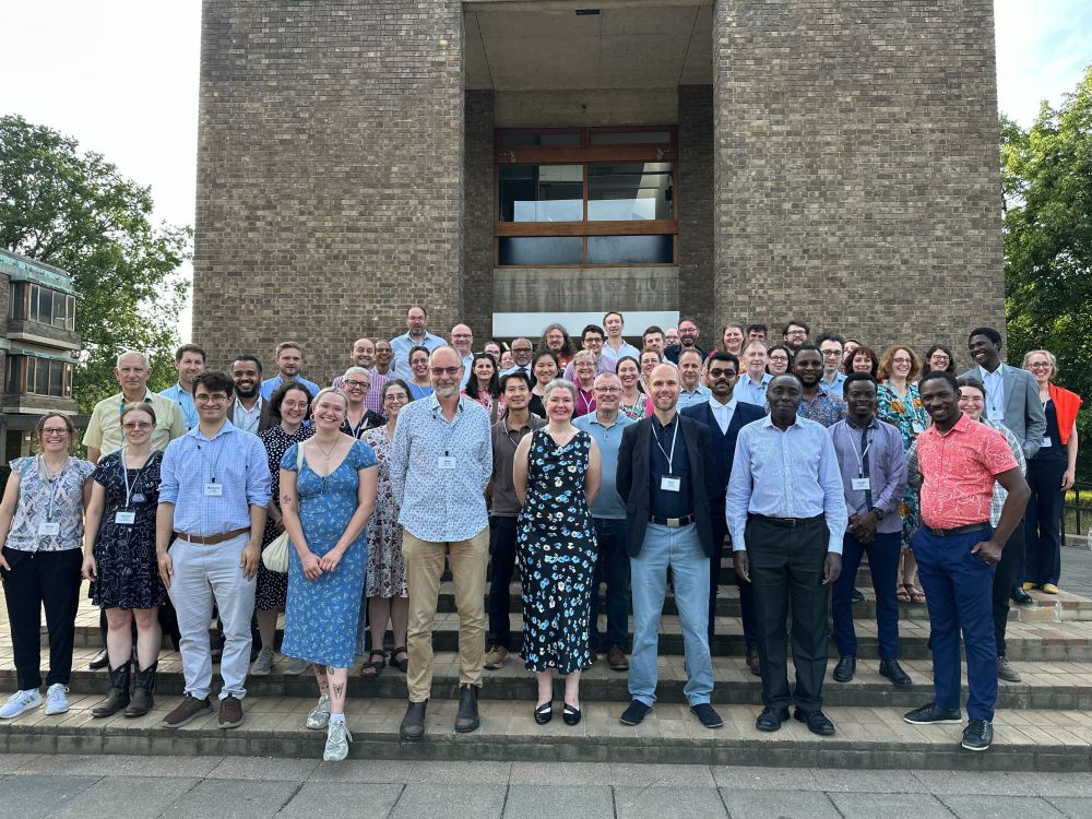 Photo of a large group of people (Isaac team and attending teachers) standing on stairs in front of Churchill college in Cambridge.