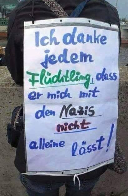 Ein Mensch, der sich mit in Plakat auf den Rücken geschnallt hat auf dem steht:
„Ich danke jedem Flüchtling, dass er mich mit den Nazis nicht alleine lässt.“