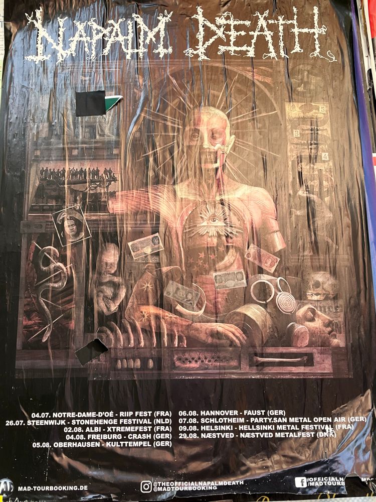 Foto von Konzertplakat der Band Napalm Death, auf dem u.A. ein gruseliger Torso abgebildet sind.