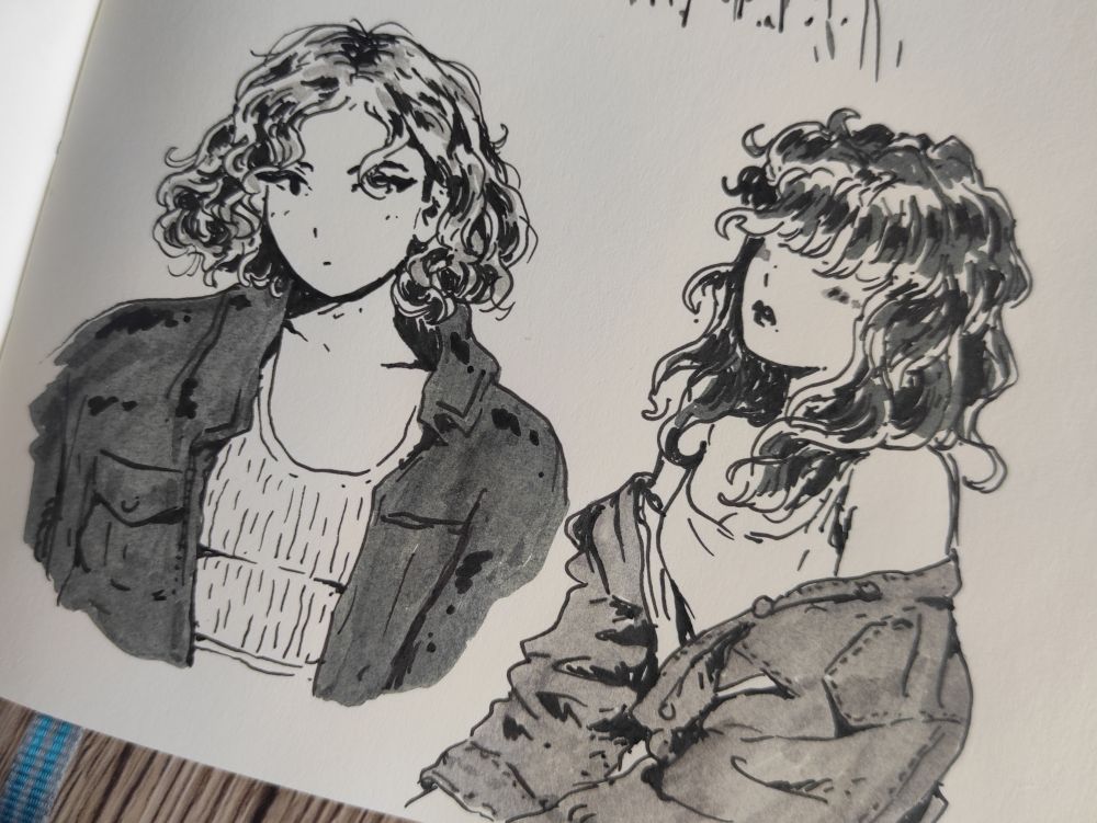 ink drawings of two woman on a part of a sketchbook page
One has a curly blonde bobcut, an oversized jacket and a crop top underneath 
The other has long curly dark hair covering her eyes, wears a tank top, and her jean jacket is loose, showing her shoulders