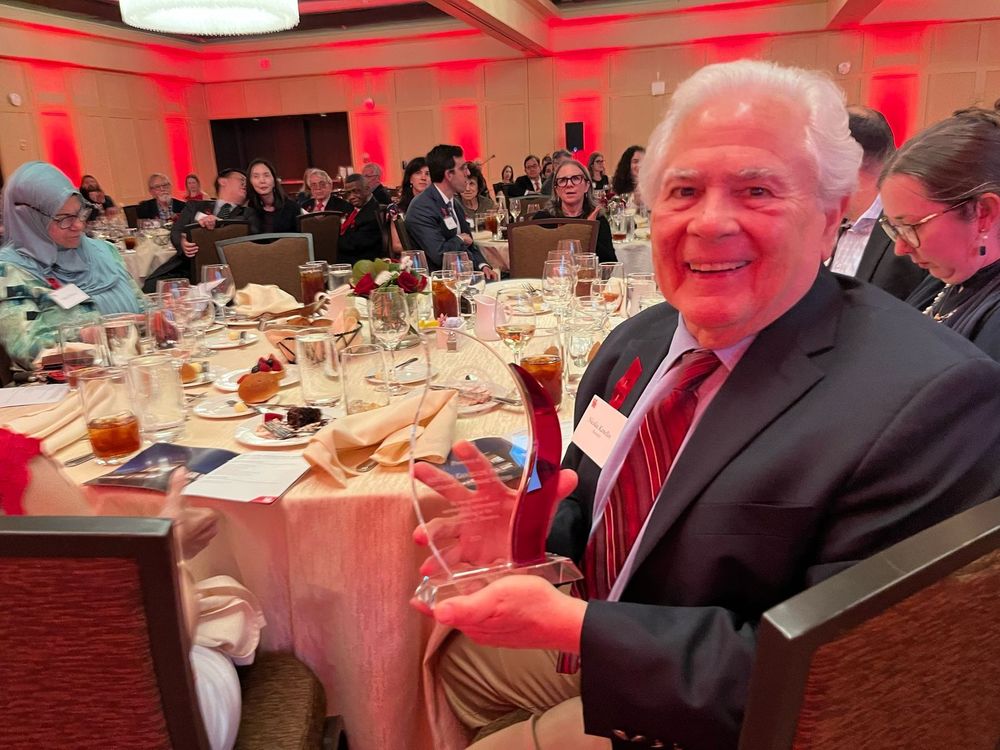 Man sitting at an event table, holding a trophy