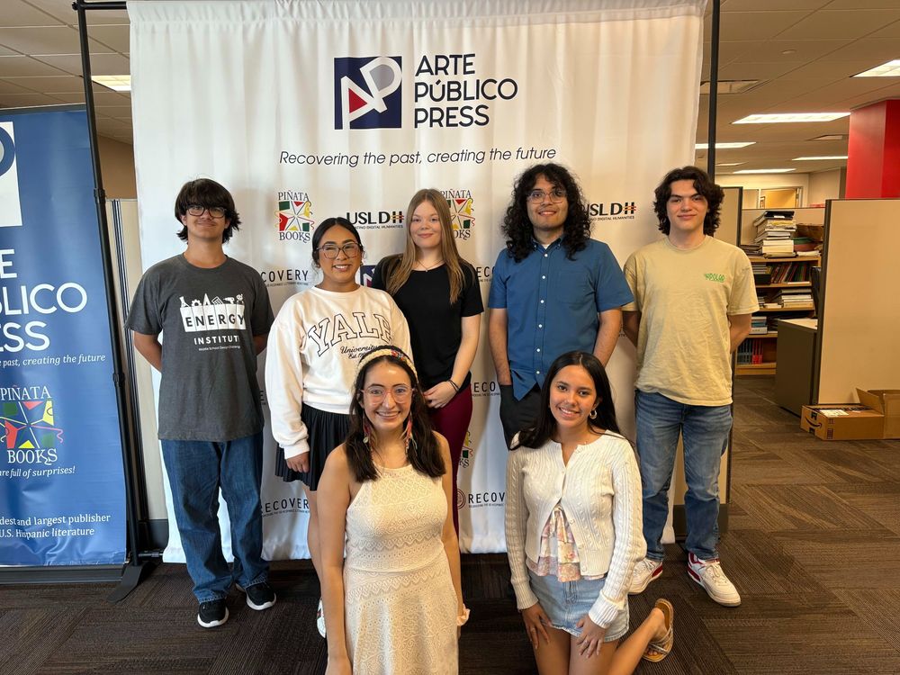 Group photo of interns posing in front of a sign with logo that reads: Arte Público Press