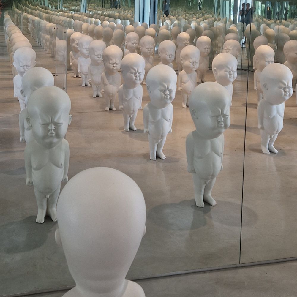 Auf dem Foto ist eine Installation zu sehen. Sie besteht aus nackten, weißen, männlichen Figuren, die grimmig schauen. Durch Spiegel wird ihr Zahl vervielfacht. 