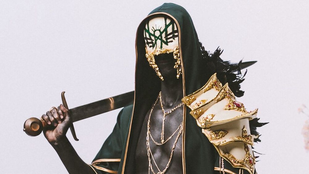 A photo of the lead singer of the band Sleep Token, Vessel. In this shot he is wearing his new armor/robes/mask and wielding a sword.