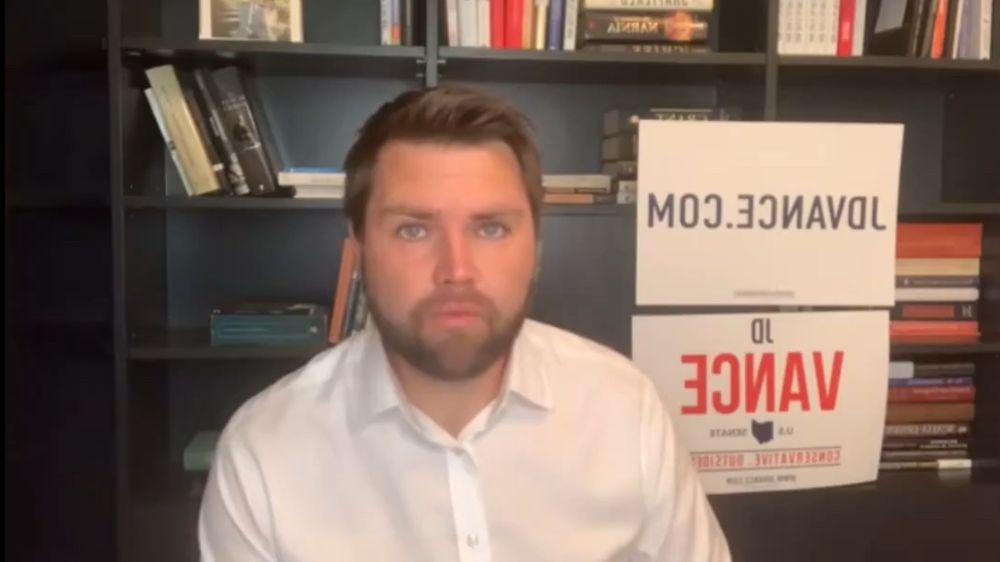 Vance on a Facebook call with signs in the background but text is mirrored 