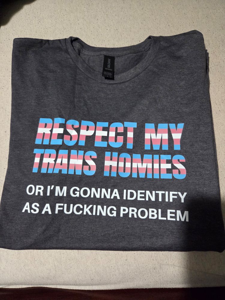 Heather gray shirt that reads "Respect my trans homies" in bold font in the colors of the trans flag, and, "or I'm gonna identify as a fucking problem" in white text below it.