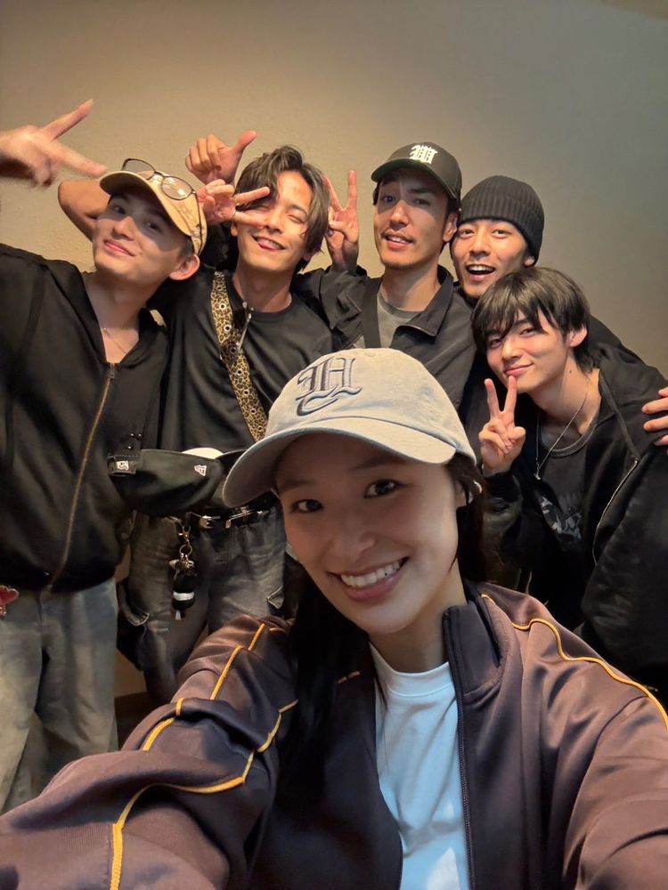 A picture of a selfie of Miu Suzuki, Yuki Hayama, Satoru Soma, Yu Miyazawa, Ryu Saito, and Haruhi Iuchi. They all previously played the main cast of Bakuage Sentai Boonboomger, with Miu Suzuki as Mira Shifuto / Bun Pink, Yuki Hayama as Ishiro Meita / Bun Blue, Satoru Soma as Genba Bureki / Bun Orange, Yu Miyazawa as Sakito Homura / Bun Violet, Ryu Saito as Jyo Akuse / Bun Black, and Haruhi Iuchi as Taiya Hando / Bun Red. They are all smiling and doing poses with their hands like a peace sign and a thumbs up.
