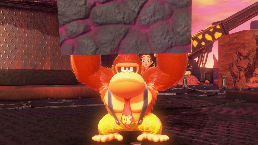 A still image from Donkey Kong Bananza, Donkey Kong holds a chunk of explosive rock while having a humorously serious face on, while Pauline's face is seen in between Donkey Kong's head and left arm, having a wide-eyed expression.