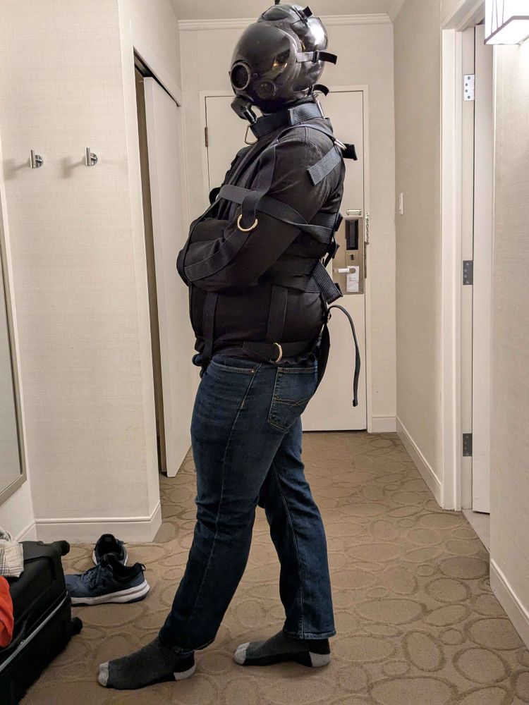 The real Tau wearing a black straitjacket, latex hood, and gas mask. Striking a pose as best as they can without arms.