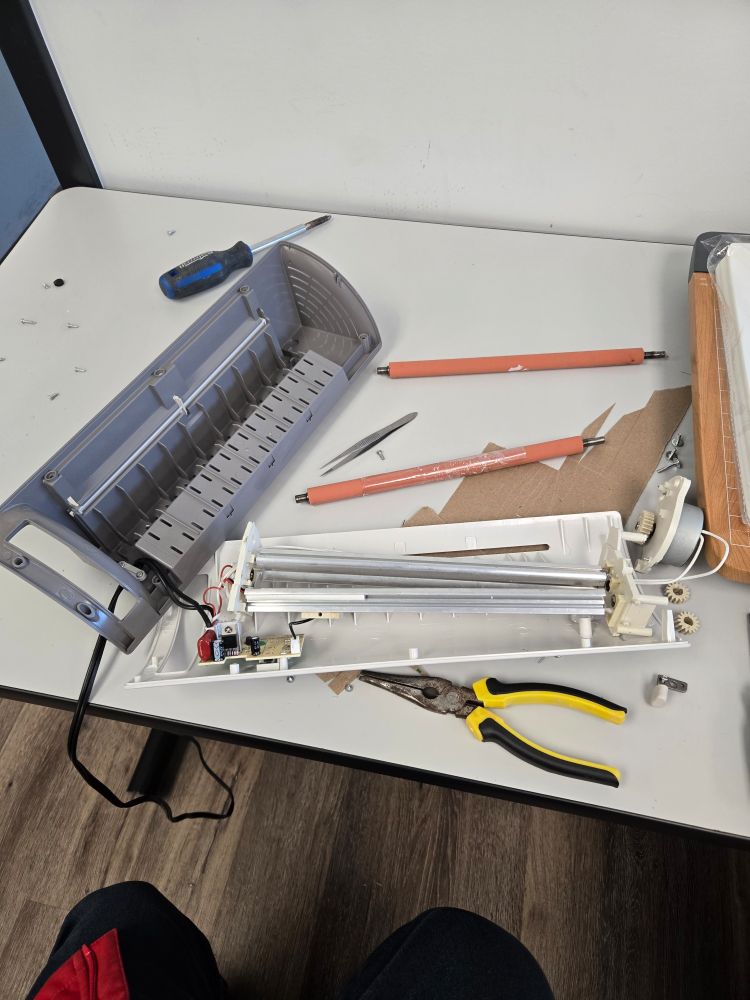 A disassembled laminating machine, with tools, parts, and newly dislodged foreign objects