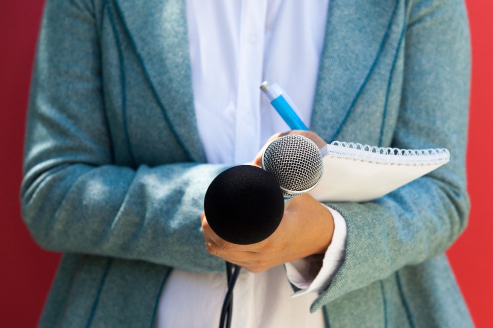 A journalist at news conference, writing notes and a holding microphone