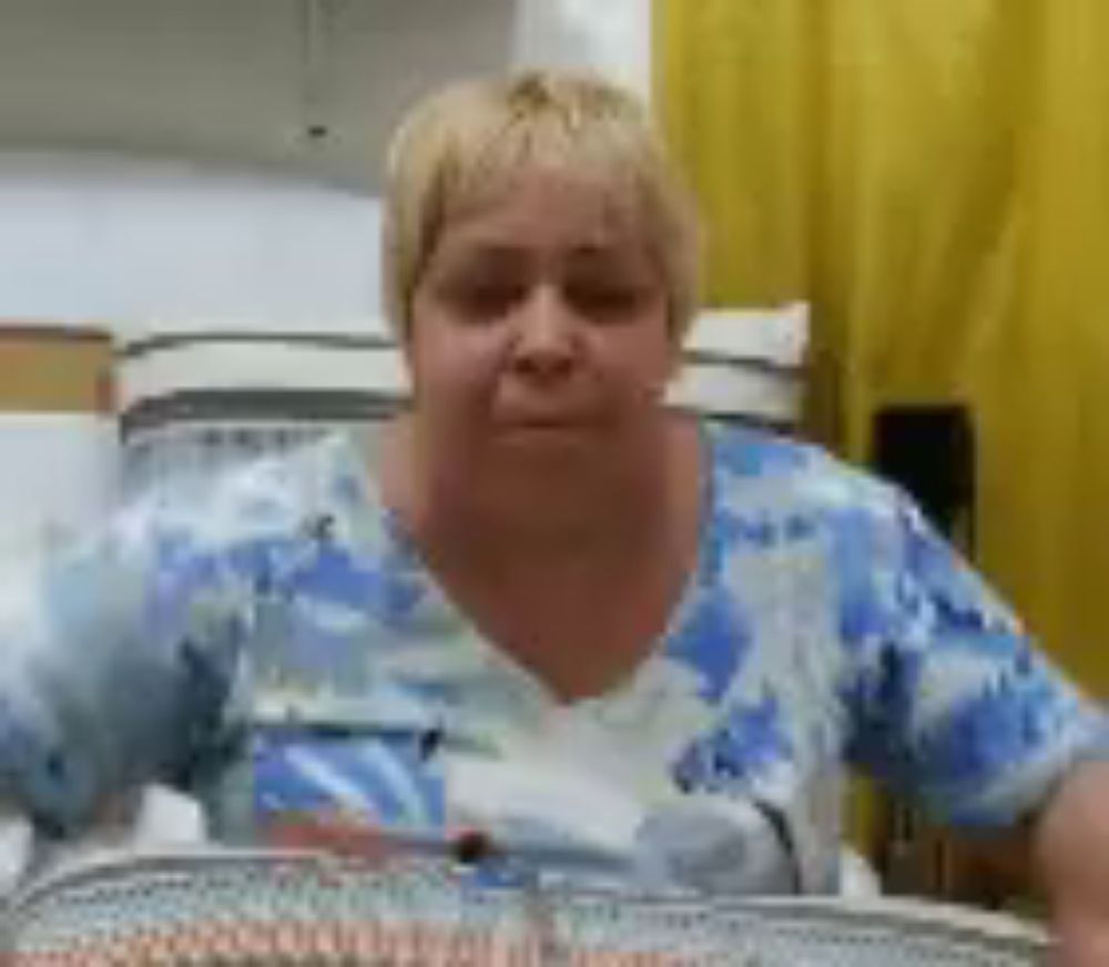 a woman in a blue and white shirt is sitting in front of a yellow curtain