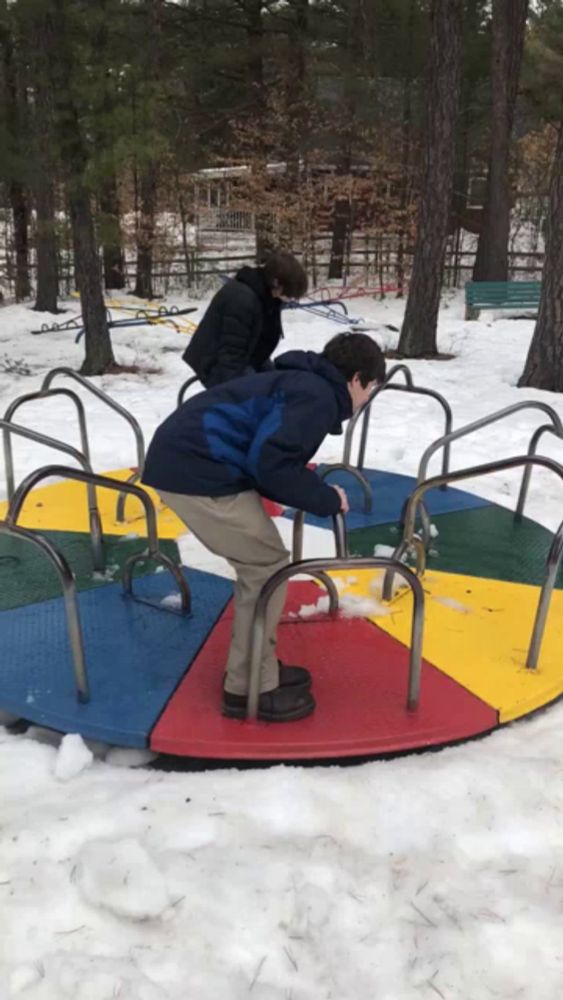 a boy in a blue jacket is standing on a colorful merry go round in the snow