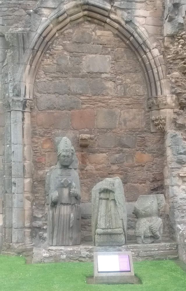 Framed by a filled-in archway in the ruins of Elgin Cathedral stands, at ground level, a statue of a bishop. He is depicted in full Mass vestments: mitre, alb and chasuble. What remains of his crozier is a staff in his left hand.