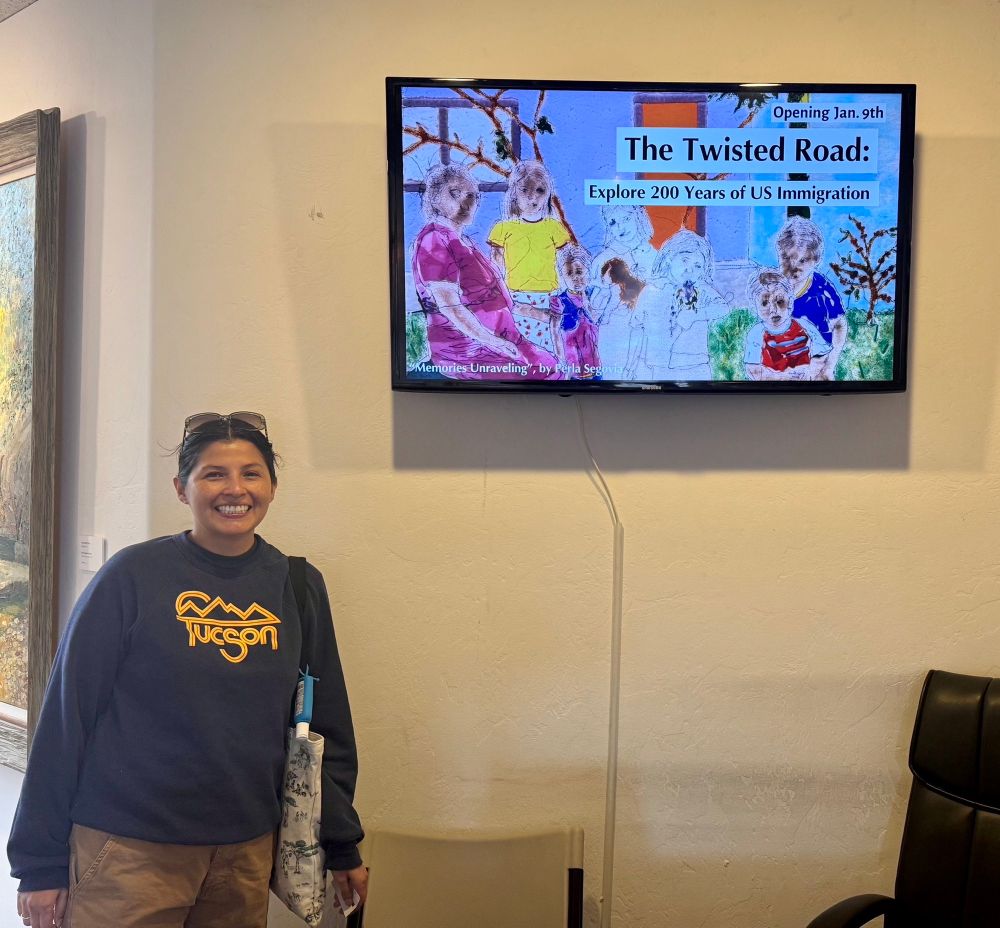 The artist Perla Segovia is standing next to a screen monitor that displays one of her works in glass and it has in writing the title of the exhibition, The Twisted Road.