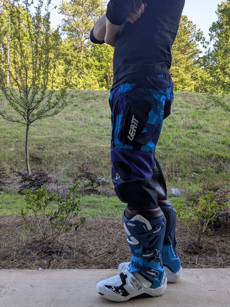 Cobalt standing outside on a concrete patio. He's wearing his Leatt pants and boots, facing towards the left of the screen with his arms crossed