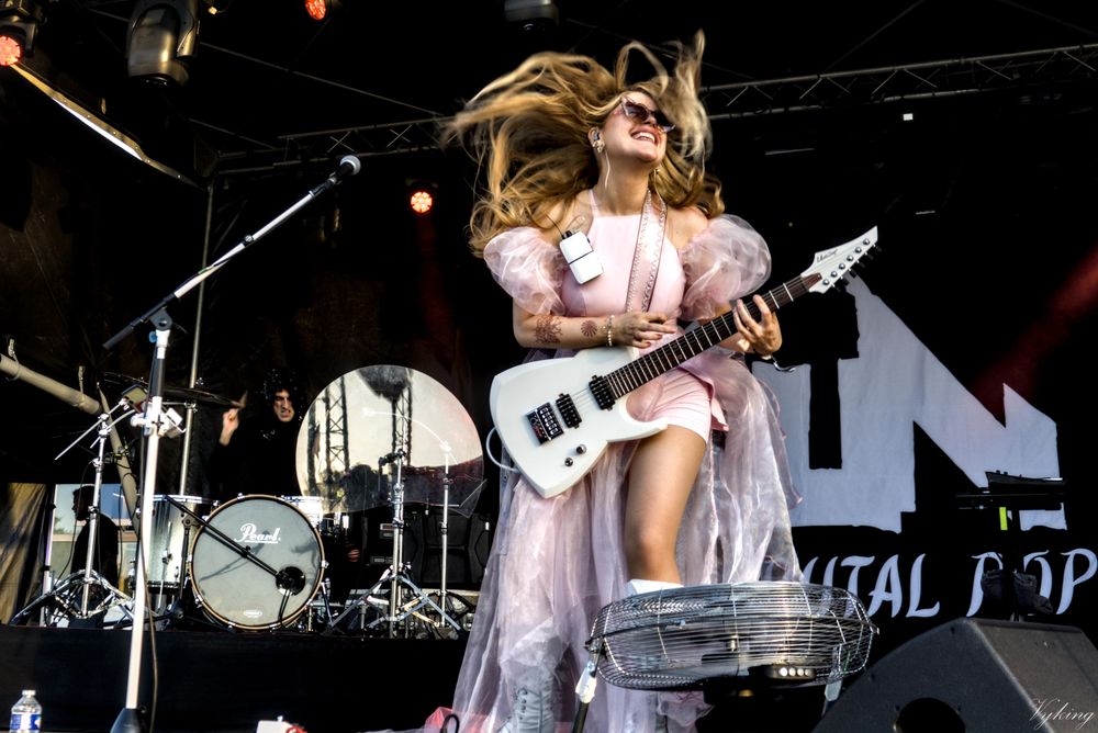 La chanteuse de Sun Brutal Pop, les cheveux libres comme l’air de grandes lunettes, un grand sourire, et une robe rose pleine de volants, et de replis en tulle. Elle joue en tapping sur sa guitare électrique blanche. À l’arrière plan, le batteur est en pleine action, avec son capuchon noir à sequins.