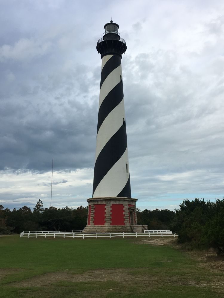 Cape Hatteras Lighthouse. A tall lighthouse with diagonal black and white stripes sits in a green field.