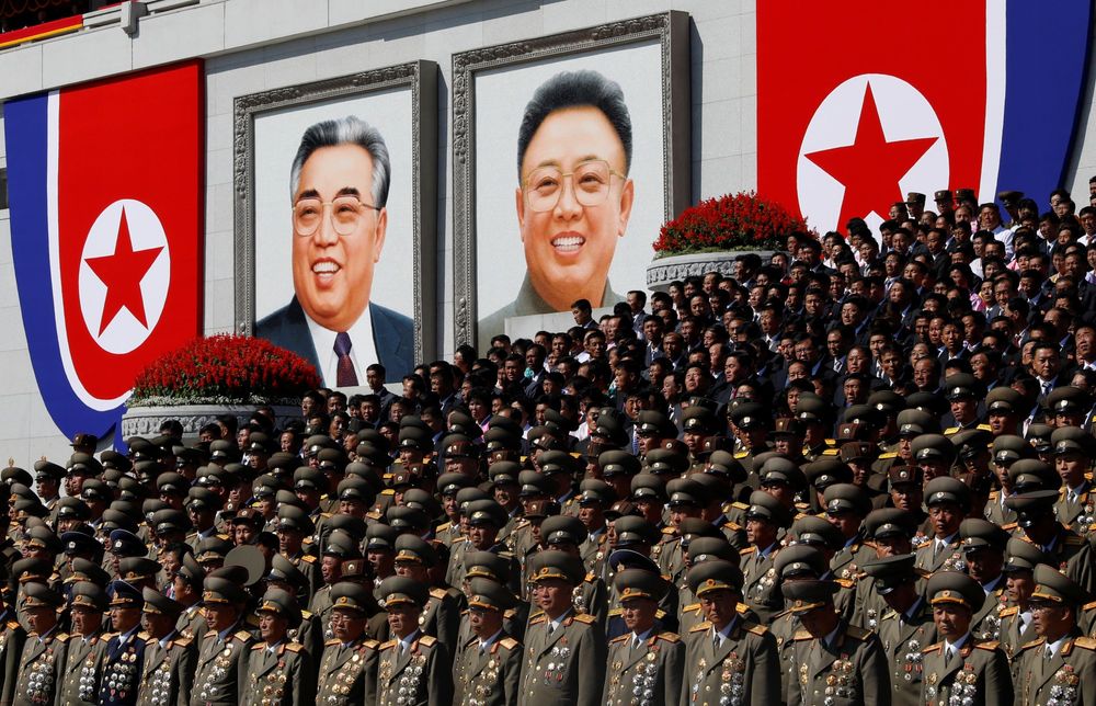 North Korean military personnel in front of NK flags as well as large format portraits of the Kims