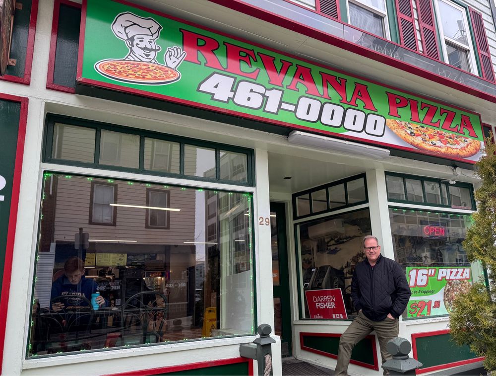 Photo of darren fisher standing next to his campaign sign at Dartmouth’s Revana Pizza