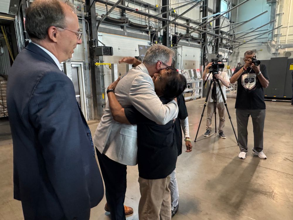 MP Fisher at the Port of Halifax hugging a member of the Africville community. Journalists with cameras are nearby. 